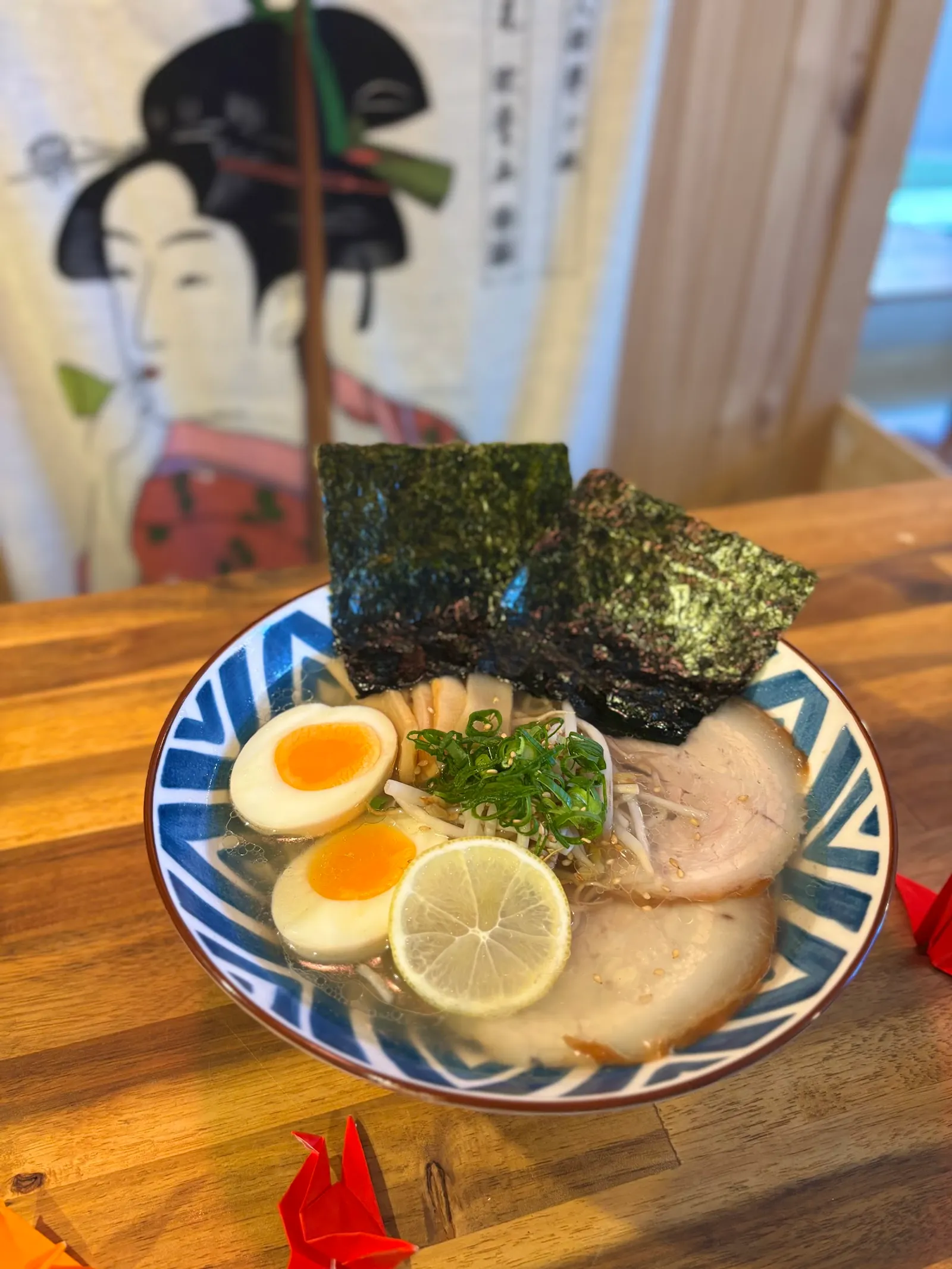 Shoyu ramen with chashu pork and nori on timber table, ukiyo-e art in background