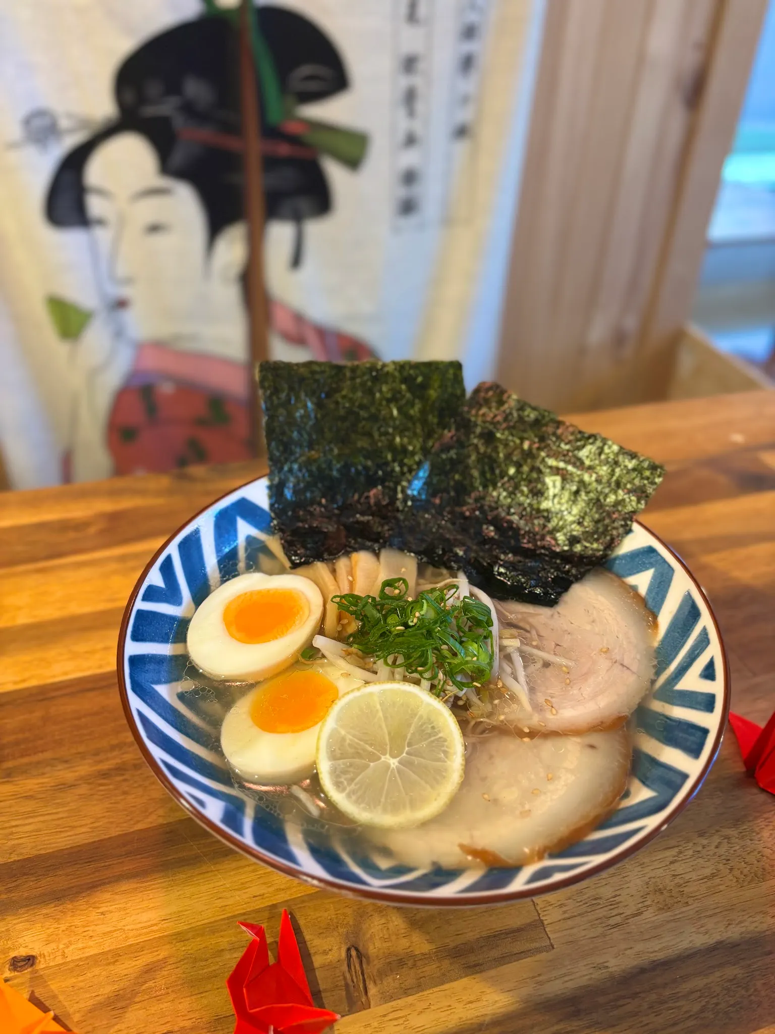Shoyu ramen with chashu pork and nori on timber table, ukiyo-e art in background