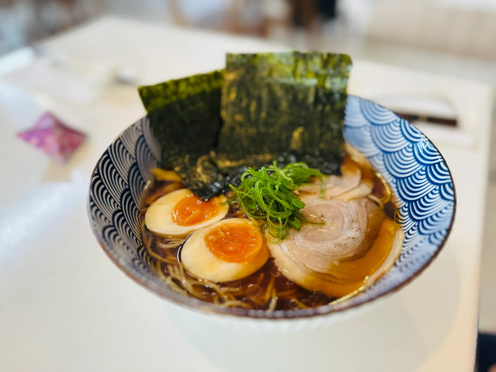 Shoyu ramen with golden broth, chashu pork and marinated eggs in blue patterned bowl
