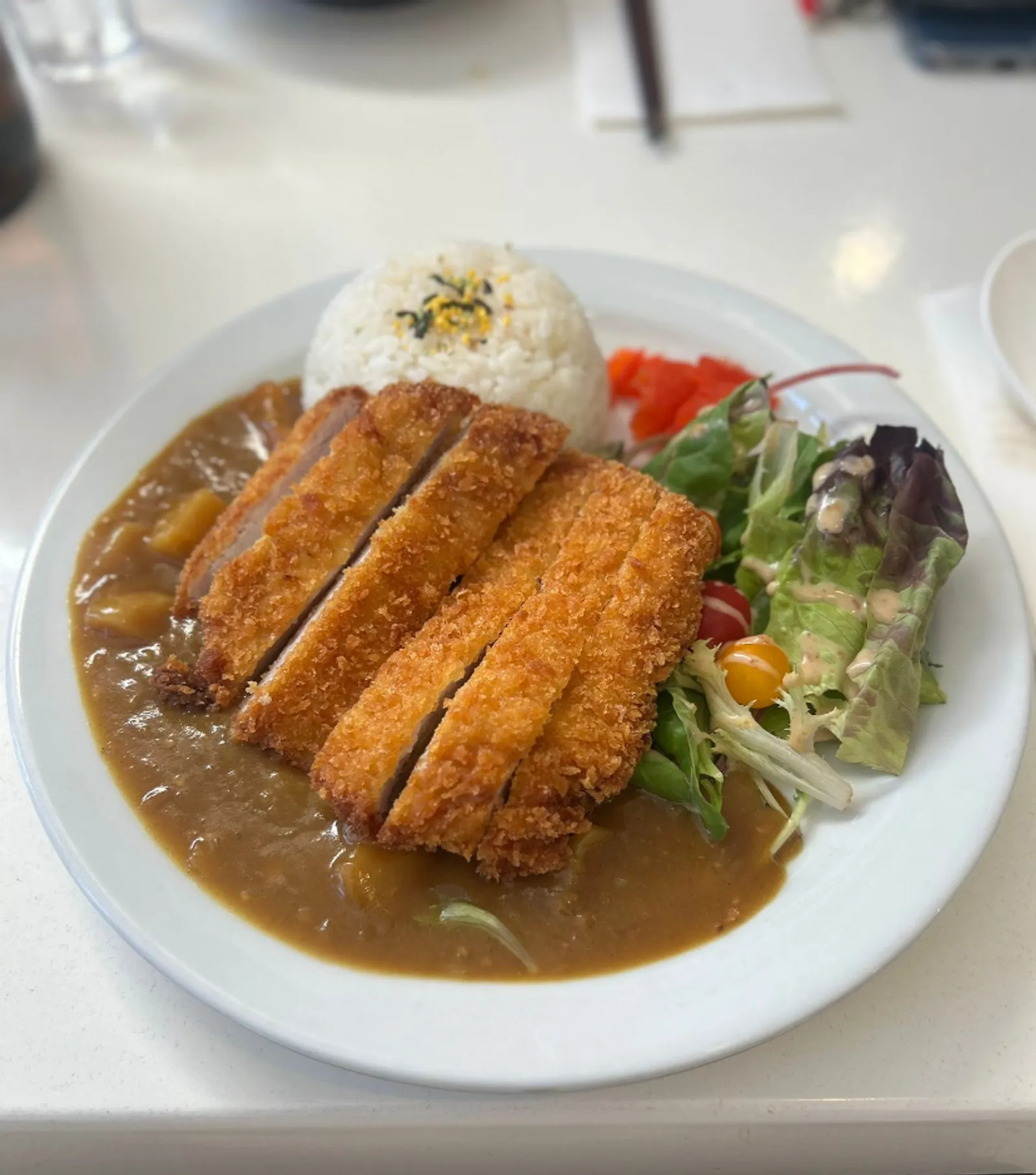 Chicken katsu curry with rice and salad on white plate