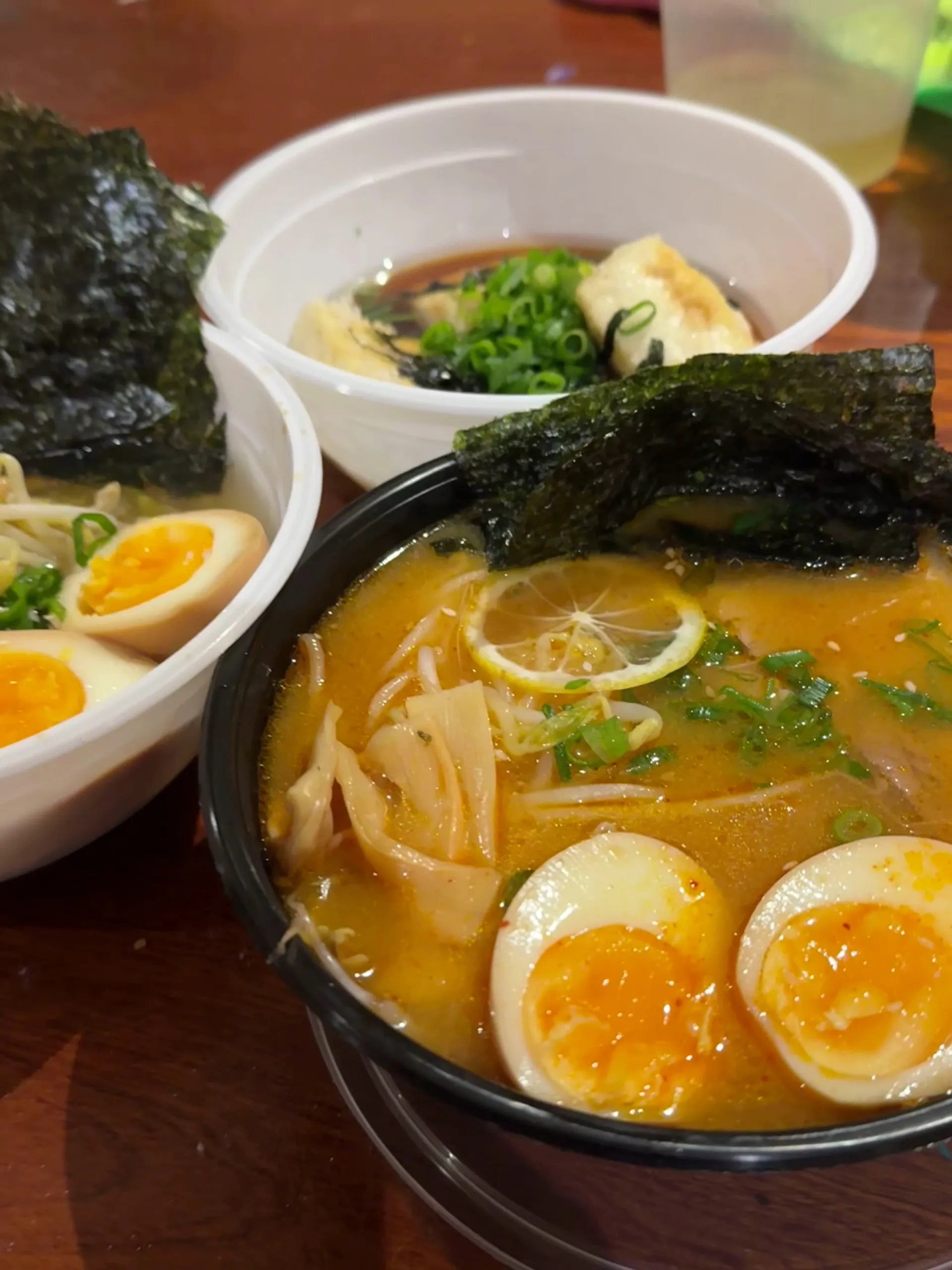 Spicy miso ramen in black bowl with side dishes on timber table