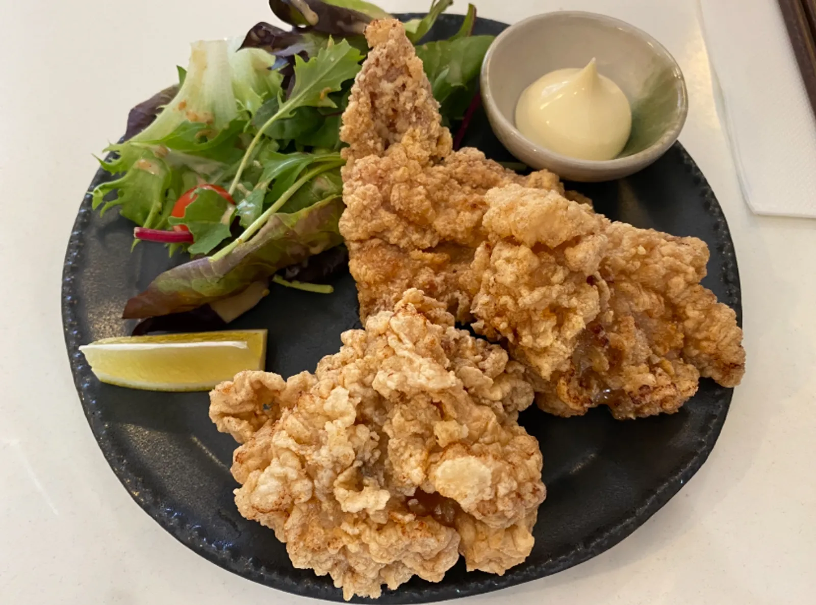 Karaage chicken with mayonnaise and lemon on dark ceramic plate