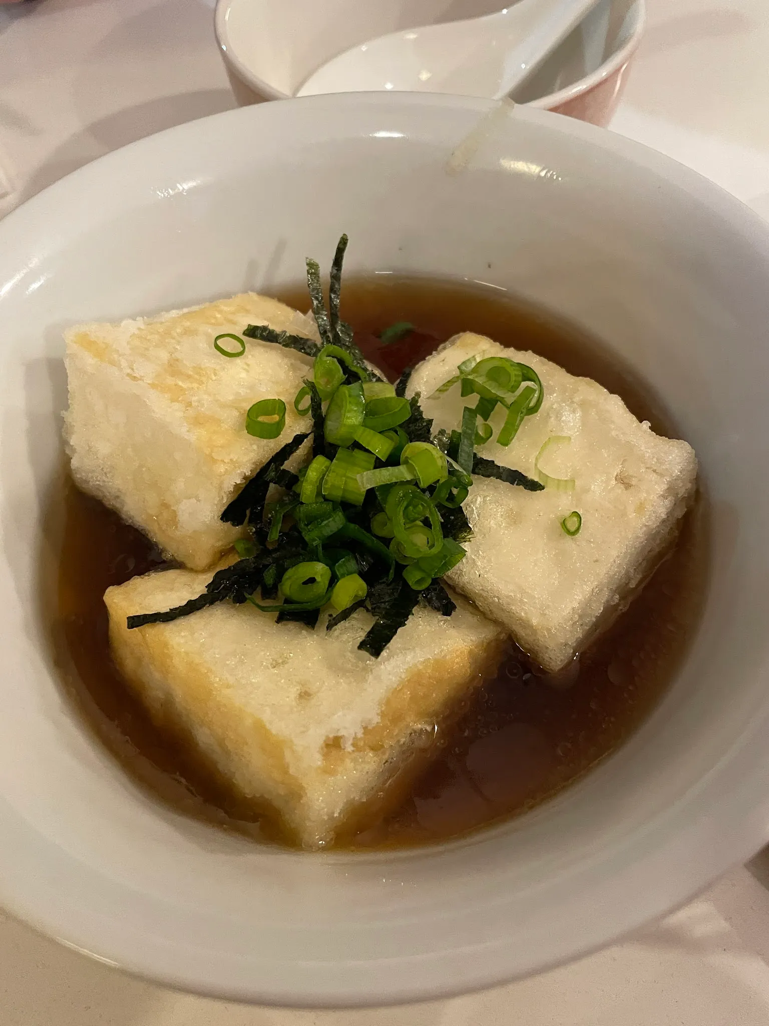 Agedashi tofu in white bowl with dashi broth and spring onion