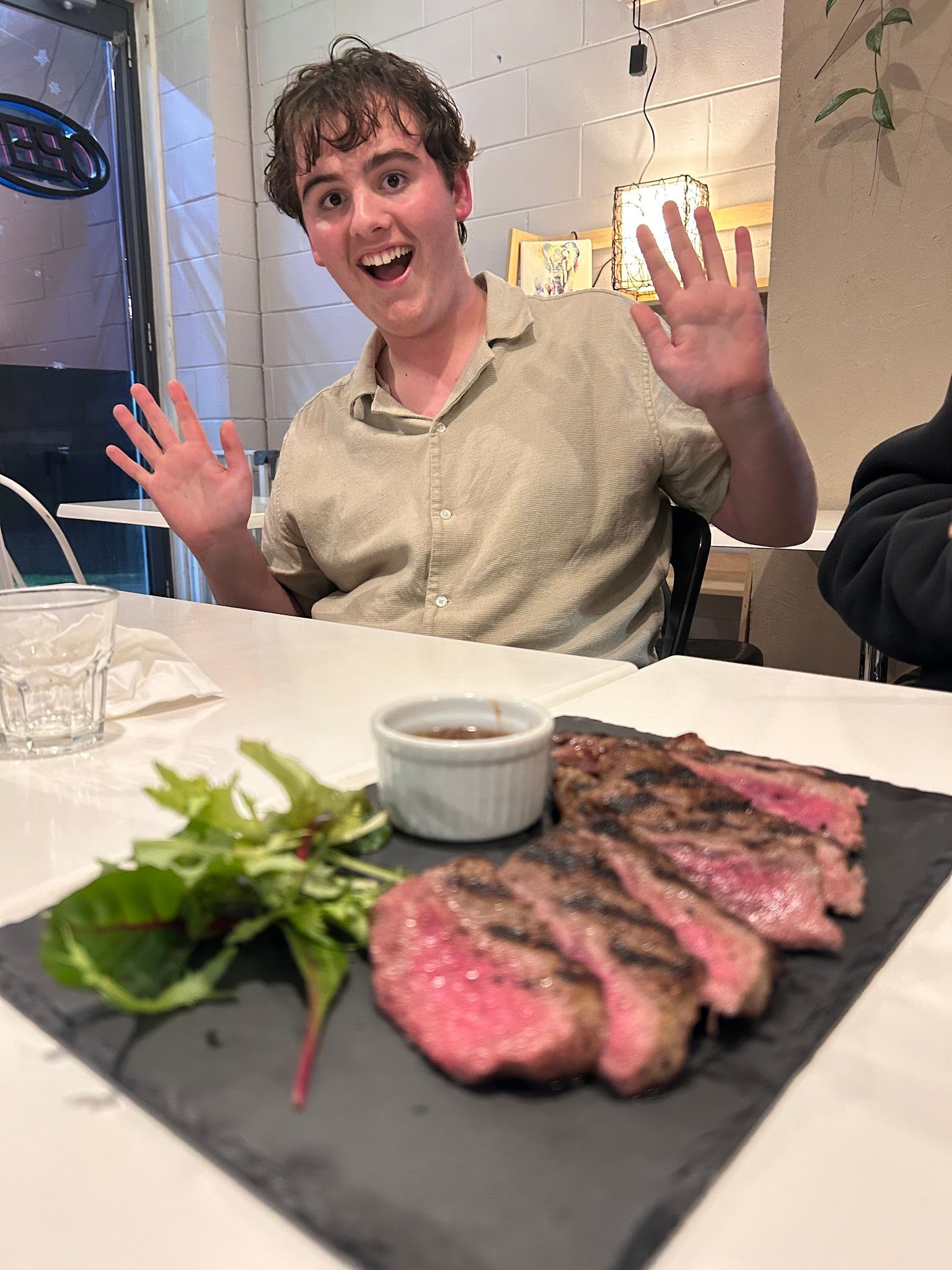 Excited diner with wagyu steak at SAYANG, white brick wall interior visible