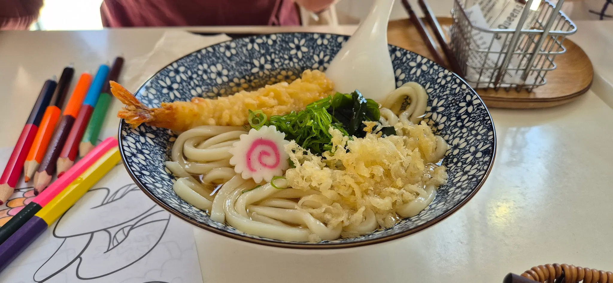 Tempura prawn udon in blue floral bowl with children's crayons beside it