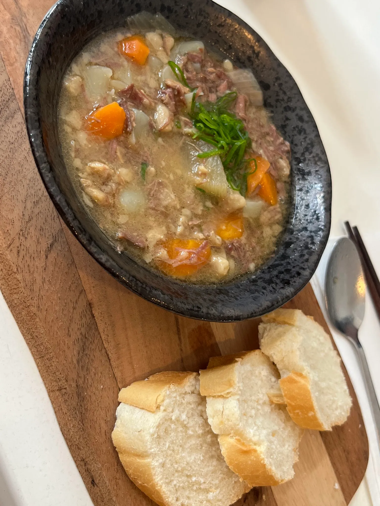 Wagyu stew in dark bowl on timber board with bread