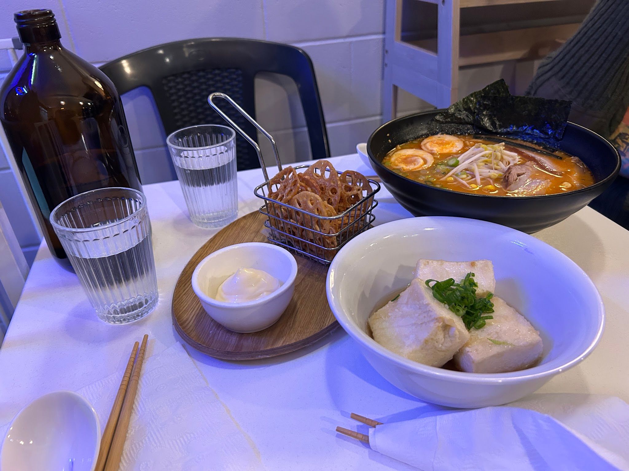 Table spread at SAYANG with ramen, renkon chips and side dishes, interior visible behind
